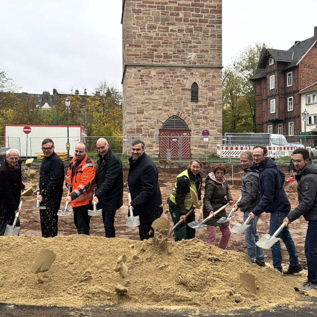 Elf Menschen, jeder mit einem Spaten ausgestattet, hinter einem Sandhaufen, beim Spatenstich für den Nikolaiplatz in Eschwege