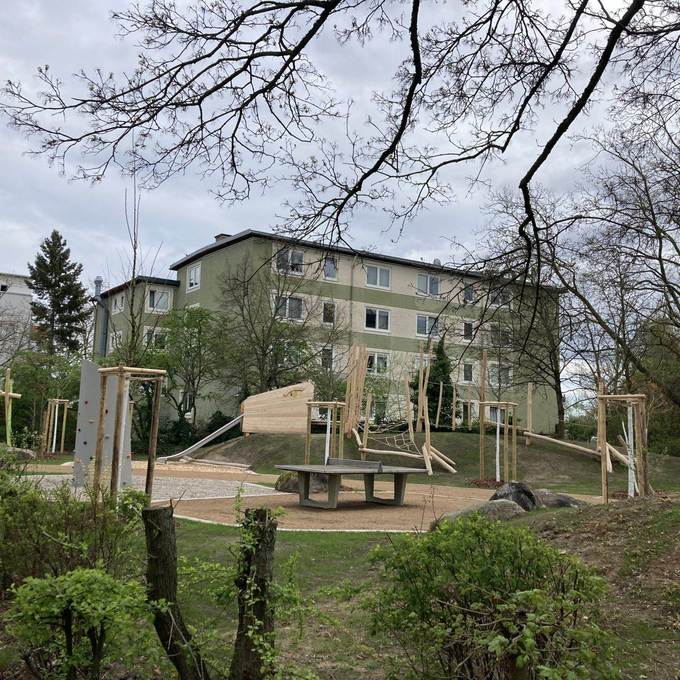 Spielplatz u.a. mit Schaukel, Kletterwand, TT-Platte und Mehrfamilienhäusern im Hintergrund