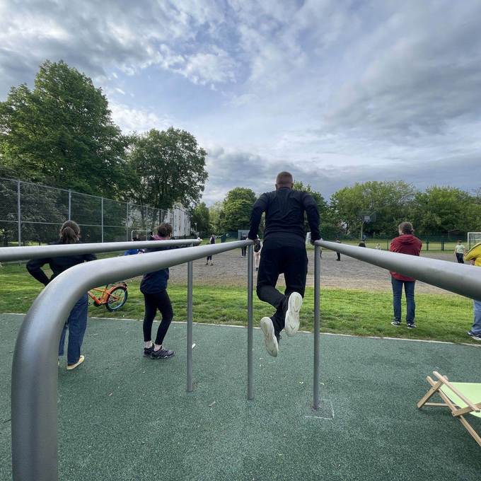 Sportgeräte in einer Parkanlage mit Menschen, die daran ihre Fitness trainieren