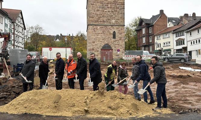 Elf Menschen mit Spaten in der Hand hinter einem Sandhaufen, hinter ihnen ein alter Turm