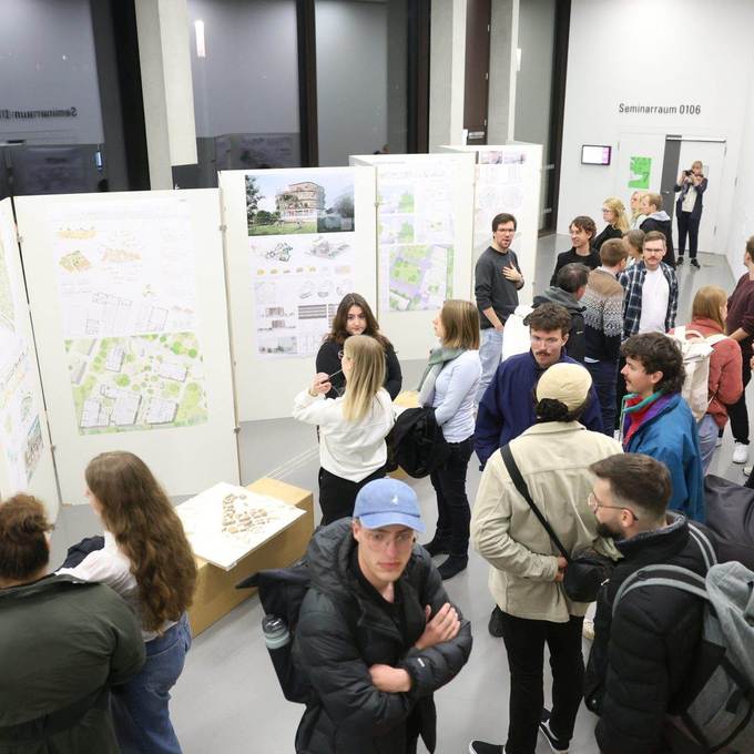 Blick von oben auf eine Gruppe von Menschen, die sich die Ausstellung der Wettbewerbsentwürfe ansieht.