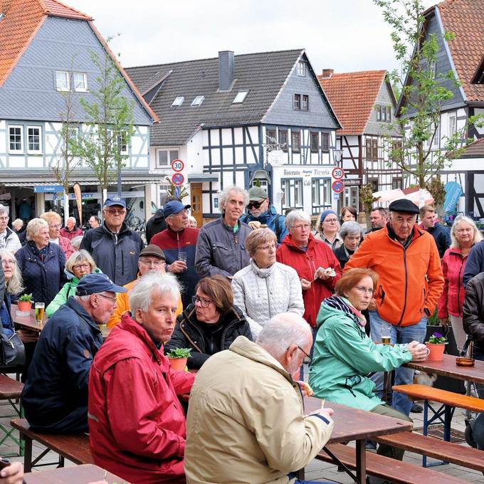 Viele Menschen sitzen auf Bänken und an Tischen vor historischer Fachwerkkulisse