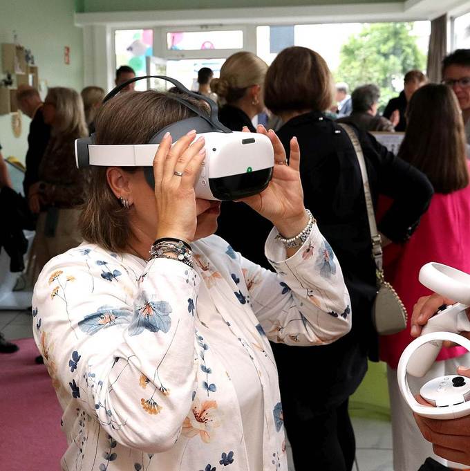 Eine Frau schaut durch eine Virtual-Reality-Brille, hinter ihr sind viele andere Menschen zu sehen